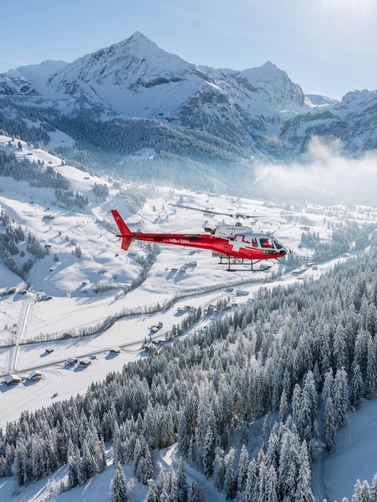 A red helicopter flying over the snow-covered Gstaad valley