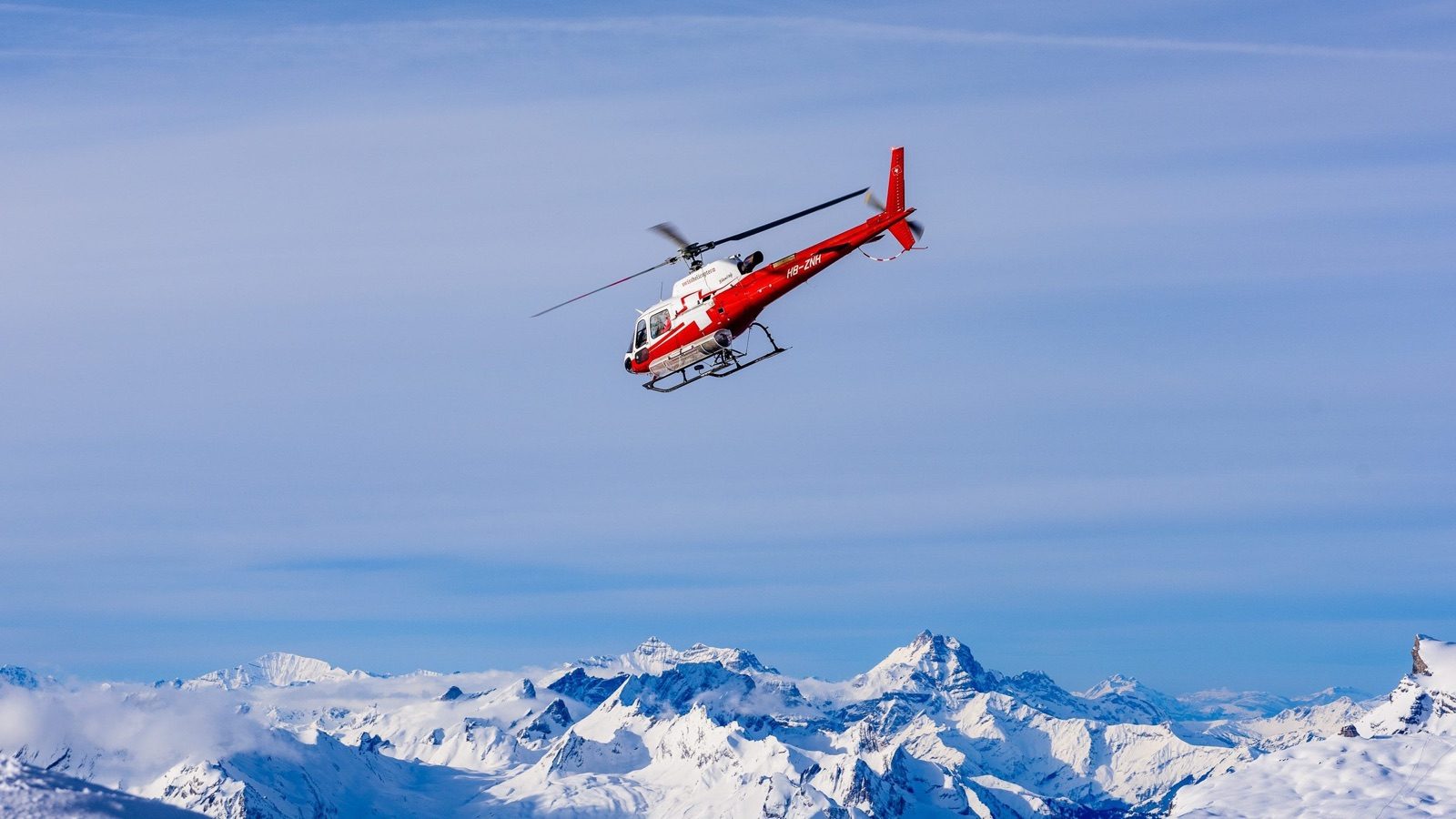 A helicopter flying above the snowy peaks around Gstaad on a heliski day