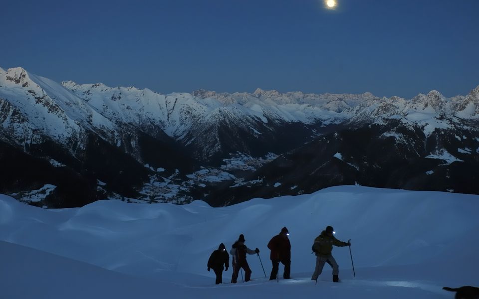 Skitourengruppe beim Aufstieg in der Abenddämmerung über dem Saanenland